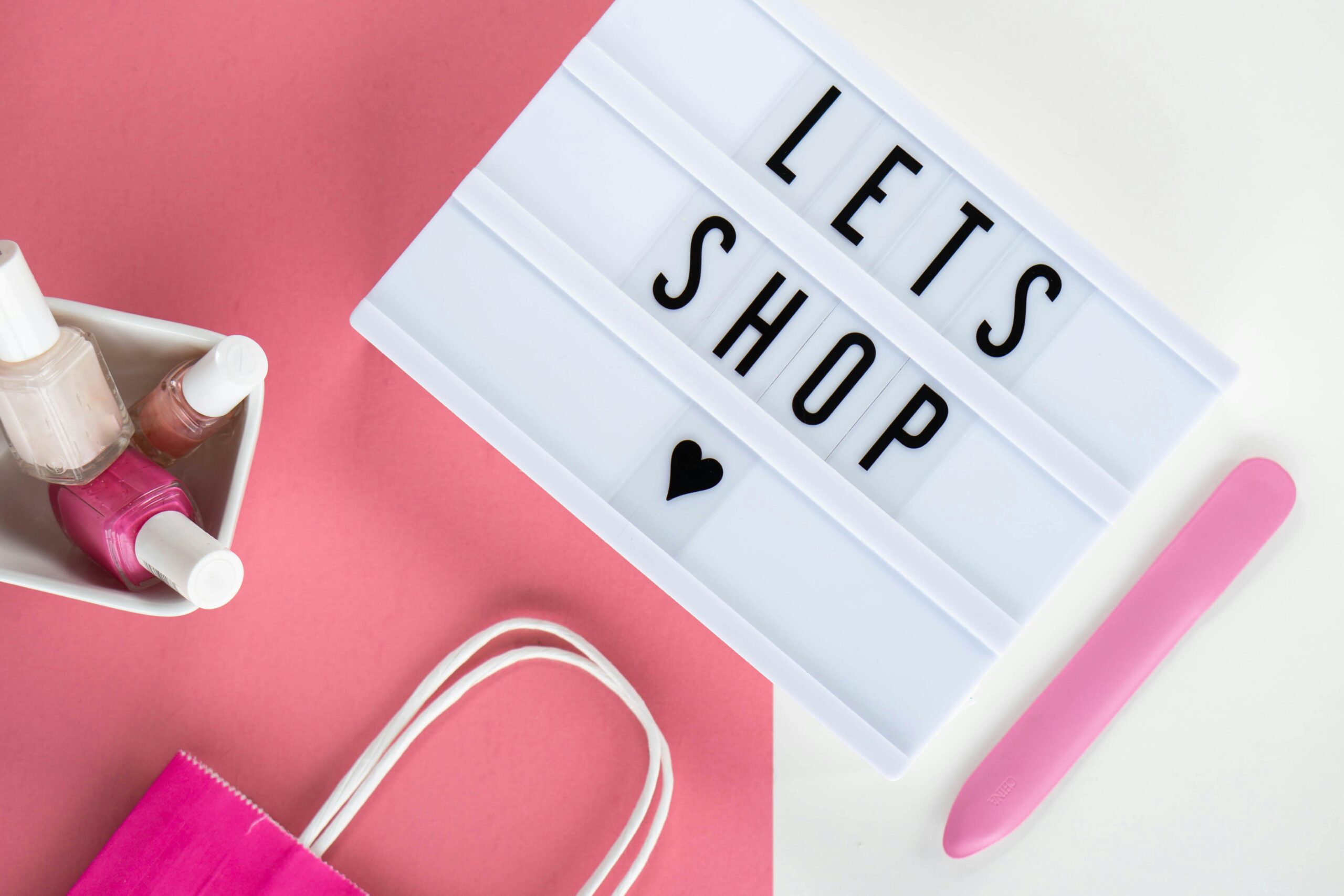 Aesthetic flat lay with a shopping theme showcasing pink accents, nail polish, and a letter board.